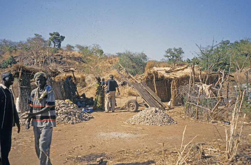 Old photo of Djouga Digs, an artisanal mining set up with grass huts and piles of rocks and hand tools
